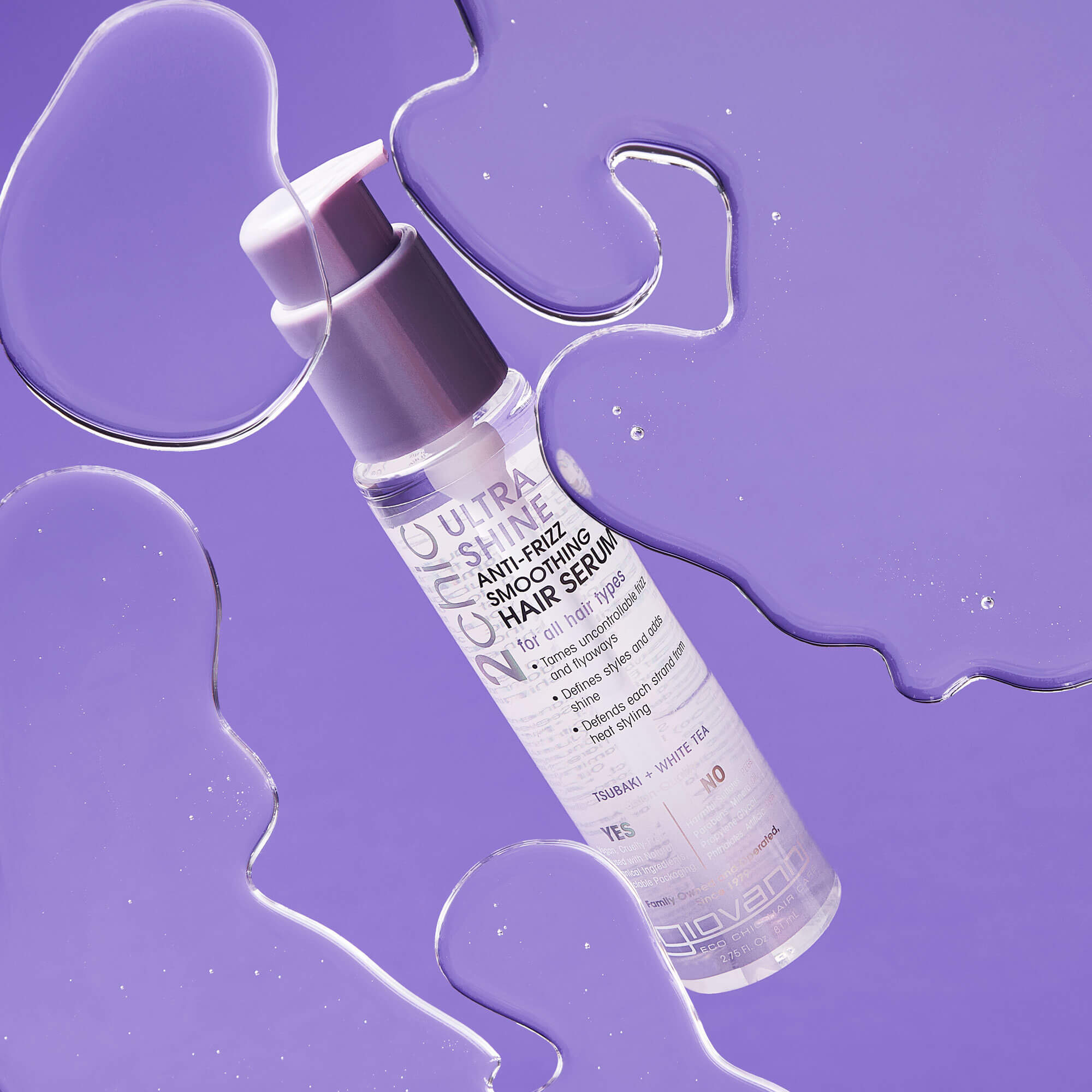 A clear bottle of Giovanni Hair Serum with a silver pump sits on a purple background, surrounded by glossy drops of liquid.