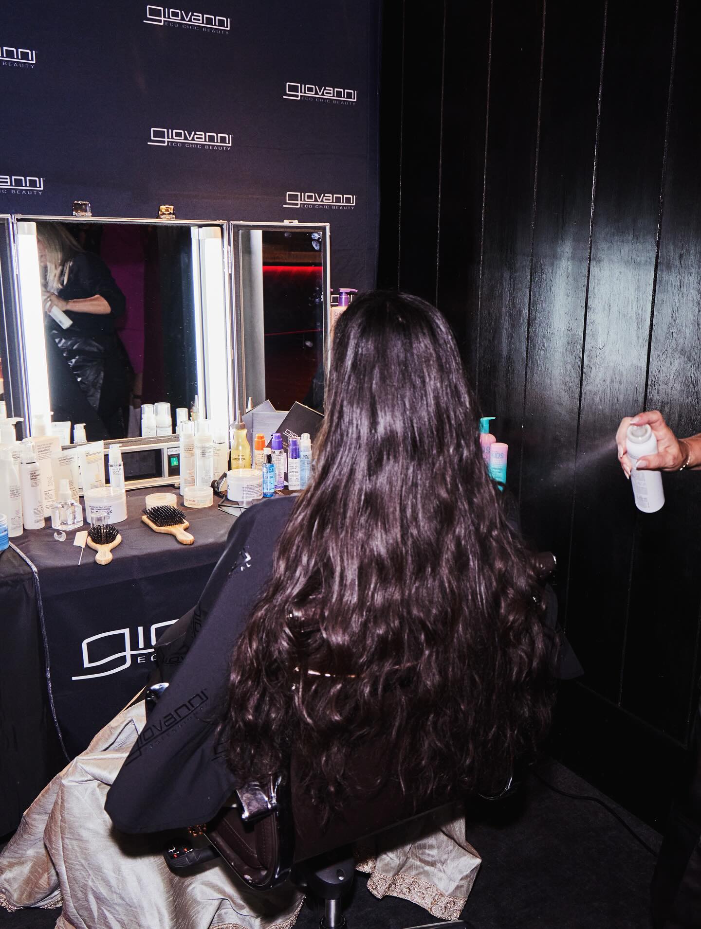 Person with long hair sitting in a chair at  a styling station with mirrors and Giovanni products.