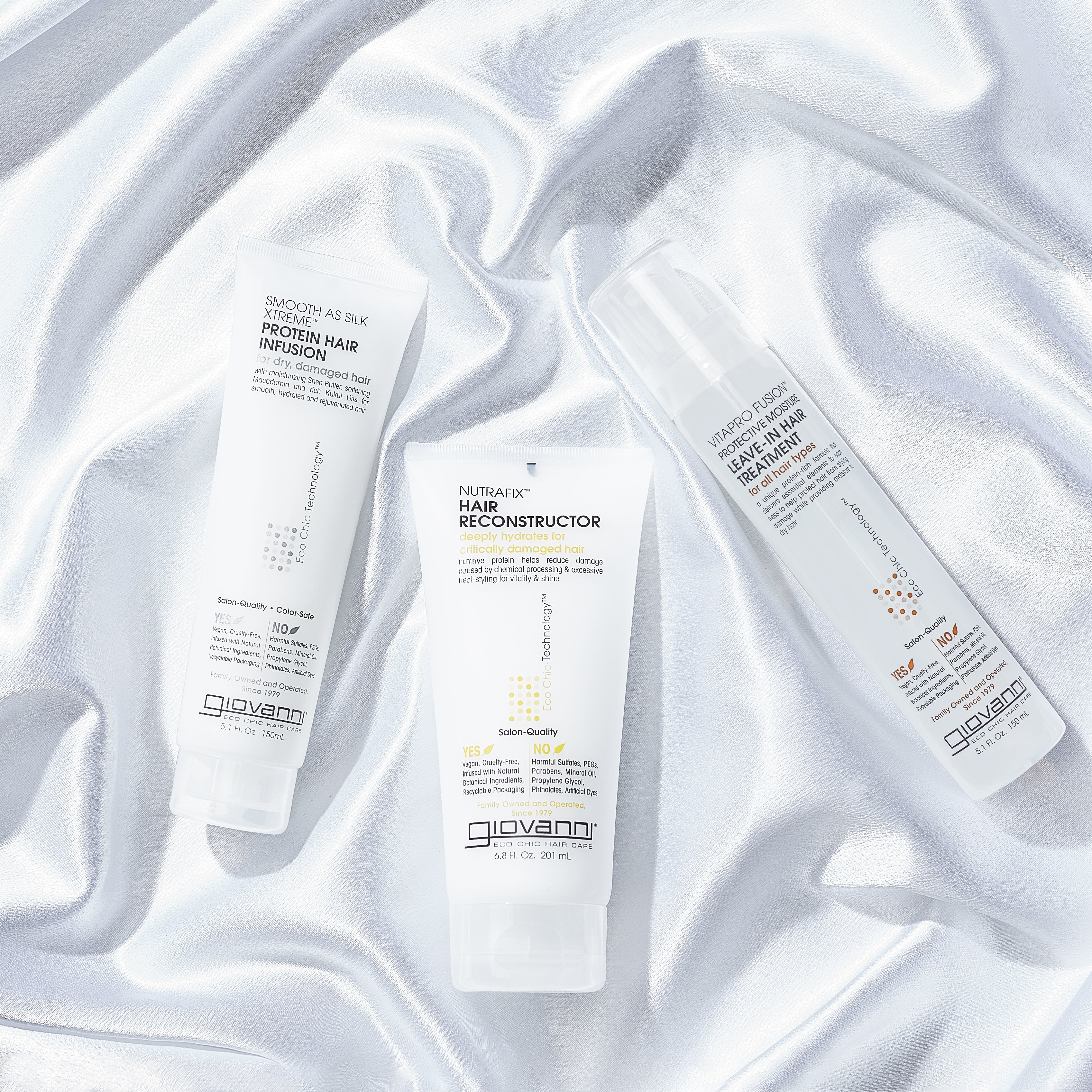 Three tubes and a spray bottle of Giovanni Cosmetics hair care, including NUTRAFIX™ HAIR RECONSTRUCTOR, are displayed on glossy white satin—ideal for color-safe, deep hair repair and nourishing treatments.