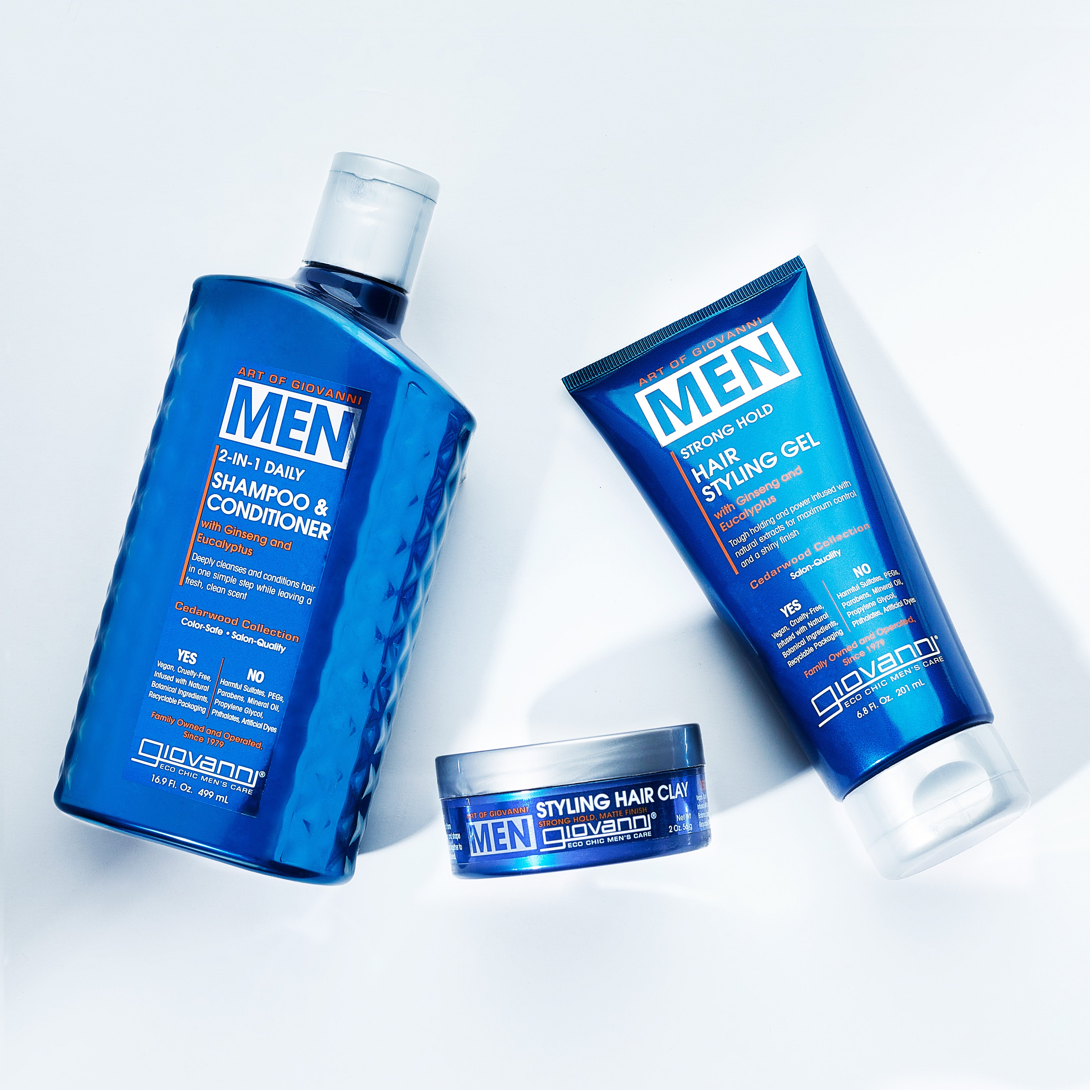 Three Giovanni Cosmetics men’s hair care products—a 2-in-1 shampoo & conditioner, strong hold styling gel, and MEN Styling Hair Clay for a matte finish—are displayed on a white background.