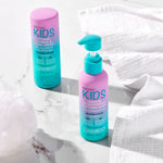 Two bottles of Giovanni Cosmetics ECO CHIC® KIDS LEAVE-IN CONDITIONING & STYLING ELIXIR sit on a white marble surface with towels nearby—perfect for tangle-free, easy hair styling in convenient teal and pink bottles.