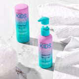 Two bottles of Giovanni Cosmetics ECO CHIC® KIDS LEAVE-IN CONDITIONING & STYLING ELIXIR sit on a white marble surface with towels nearby—perfect for tangle-free, easy hair styling in convenient teal and pink bottles.